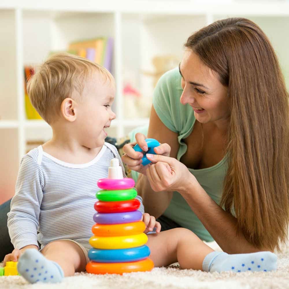 Teacher playing with ring stacking toy alongside infant